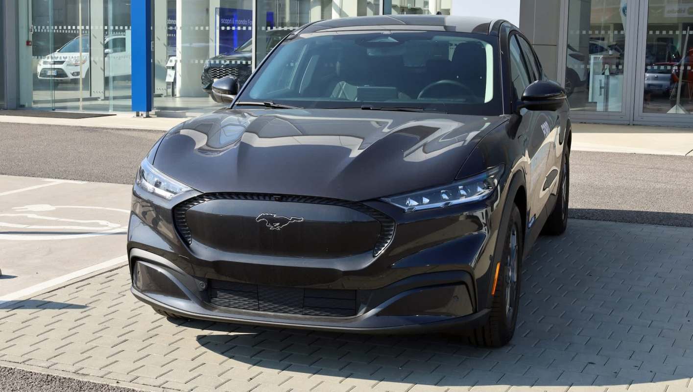 A sleek black Ford Mustang Mach-E parked outside a dealership under clear skies.