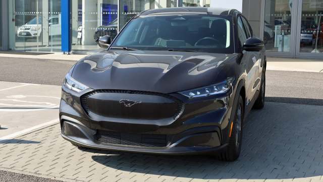 A sleek black Ford Mustang Mach-E parked outside a dealership under clear skies.
