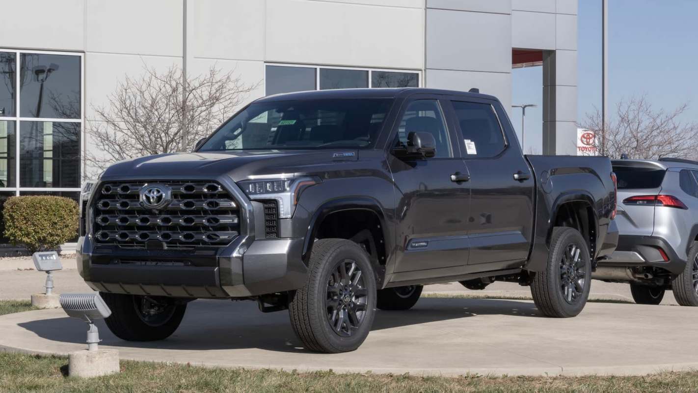A black Toyota Tundra truck parked in front of a dealership with a smaller vehicle visible in the background.