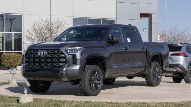 A black Toyota Tundra truck parked in front of a dealership with a smaller vehicle visible in the background.