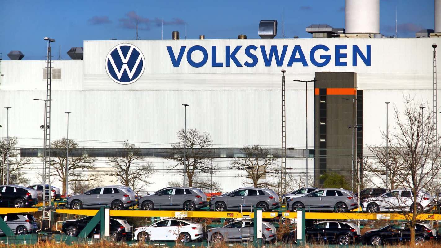 Volkswagen factory with rows of parked cars in front, showcasing the company's logo prominently on the building.