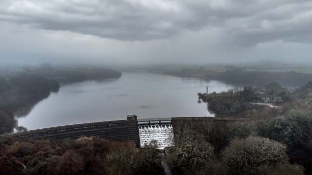 A misty sky over a reservoir and dam with flowing water.