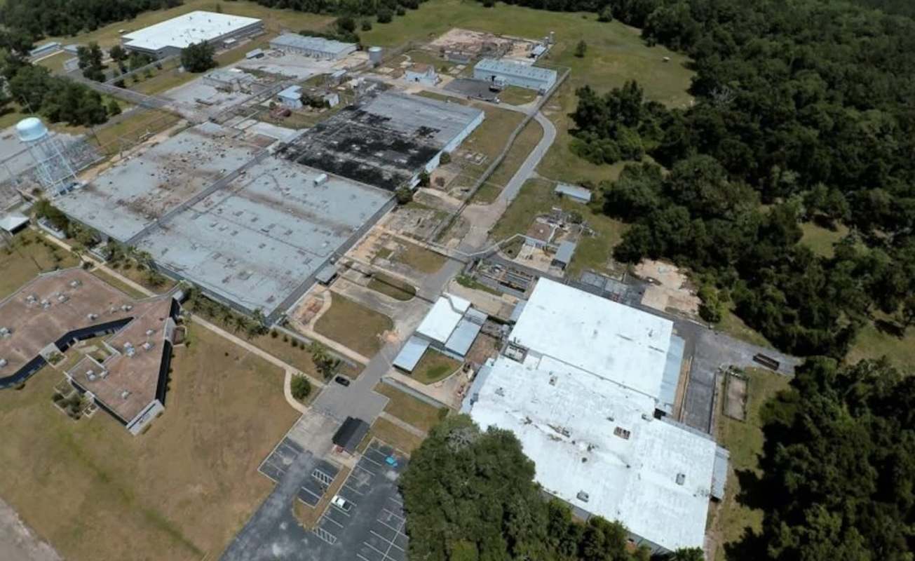 An aerial view of an abandoned industrial complex surrounded by greenery and open land.