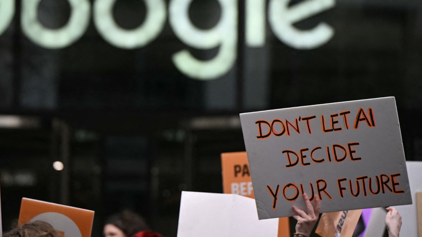 A protestor holds a "Don't let AI decide your future" sign in front of a Google office.