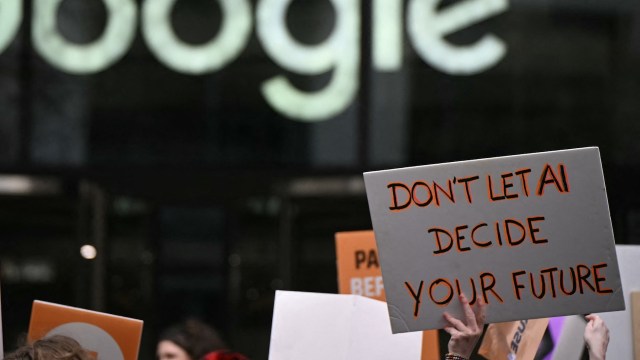 A protestor holds a "Don't let AI decide your future" sign in front of a Google office.