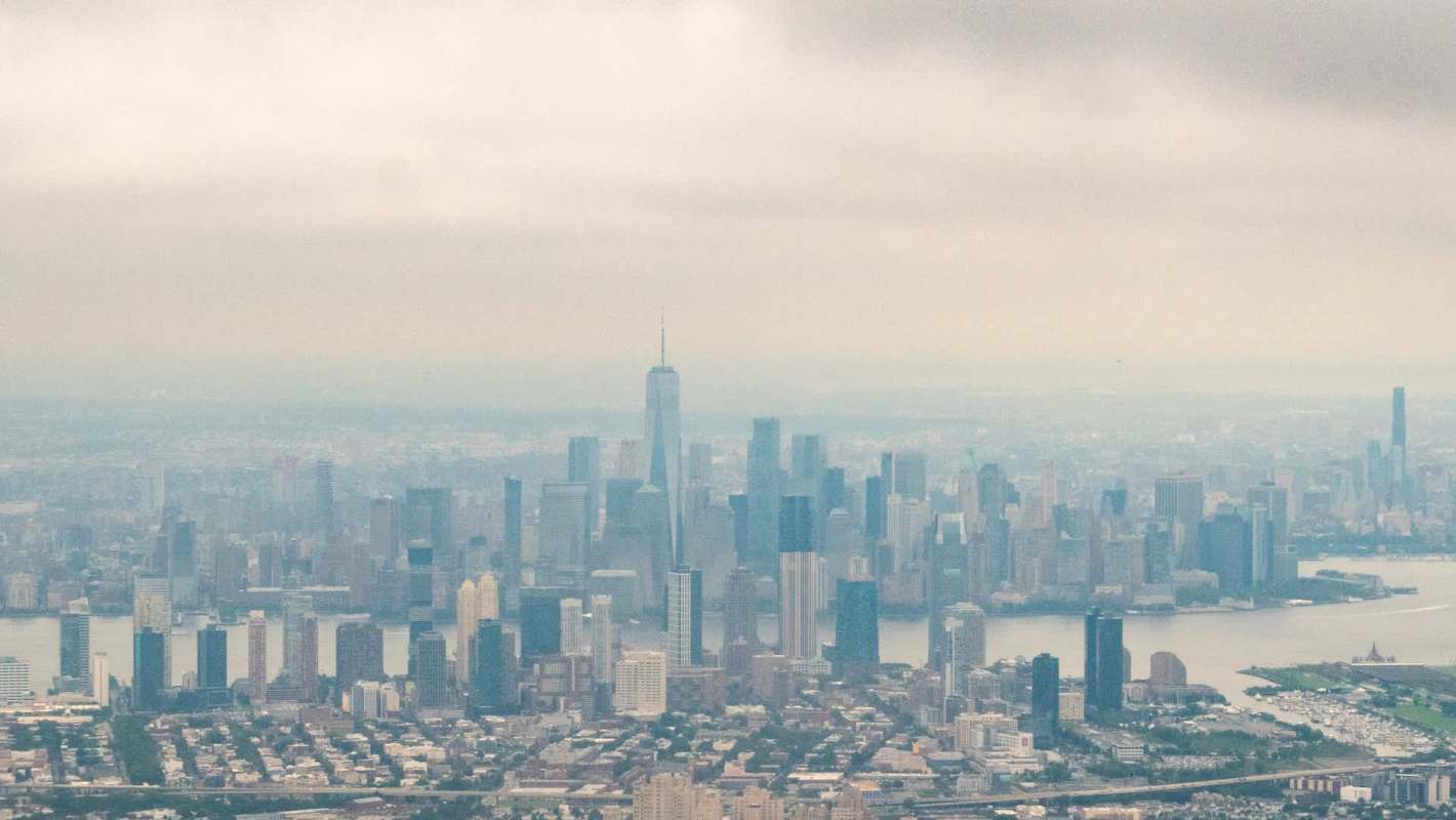 A panoramic view of the New York City skyline shrouded in smog, featuring tall skyscrapers and a river.