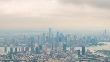 A panoramic view of the New York City skyline shrouded in smog, featuring tall skyscrapers and a river.