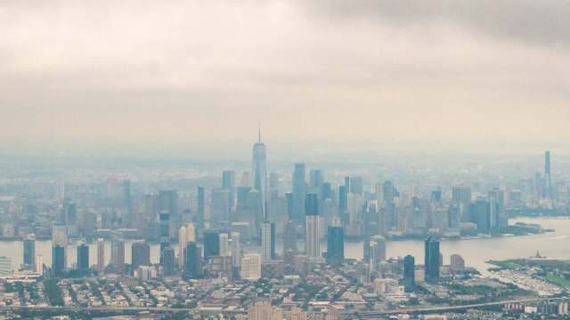 A panoramic view of the New York City skyline shrouded in smog, featuring tall skyscrapers and a river.