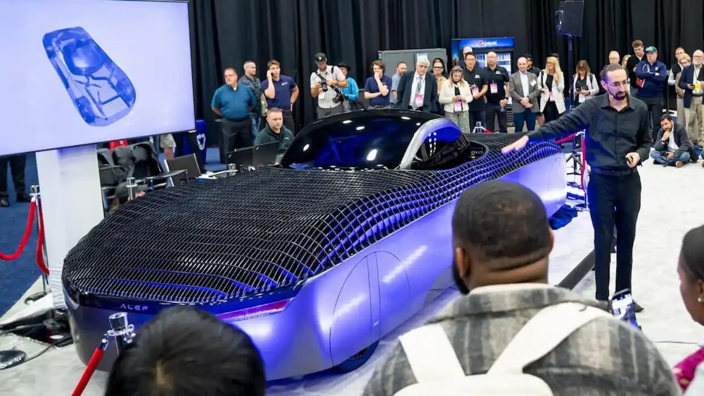 A futuristic purple electric car with a netted design is showcased at an event, surrounded by an audience.