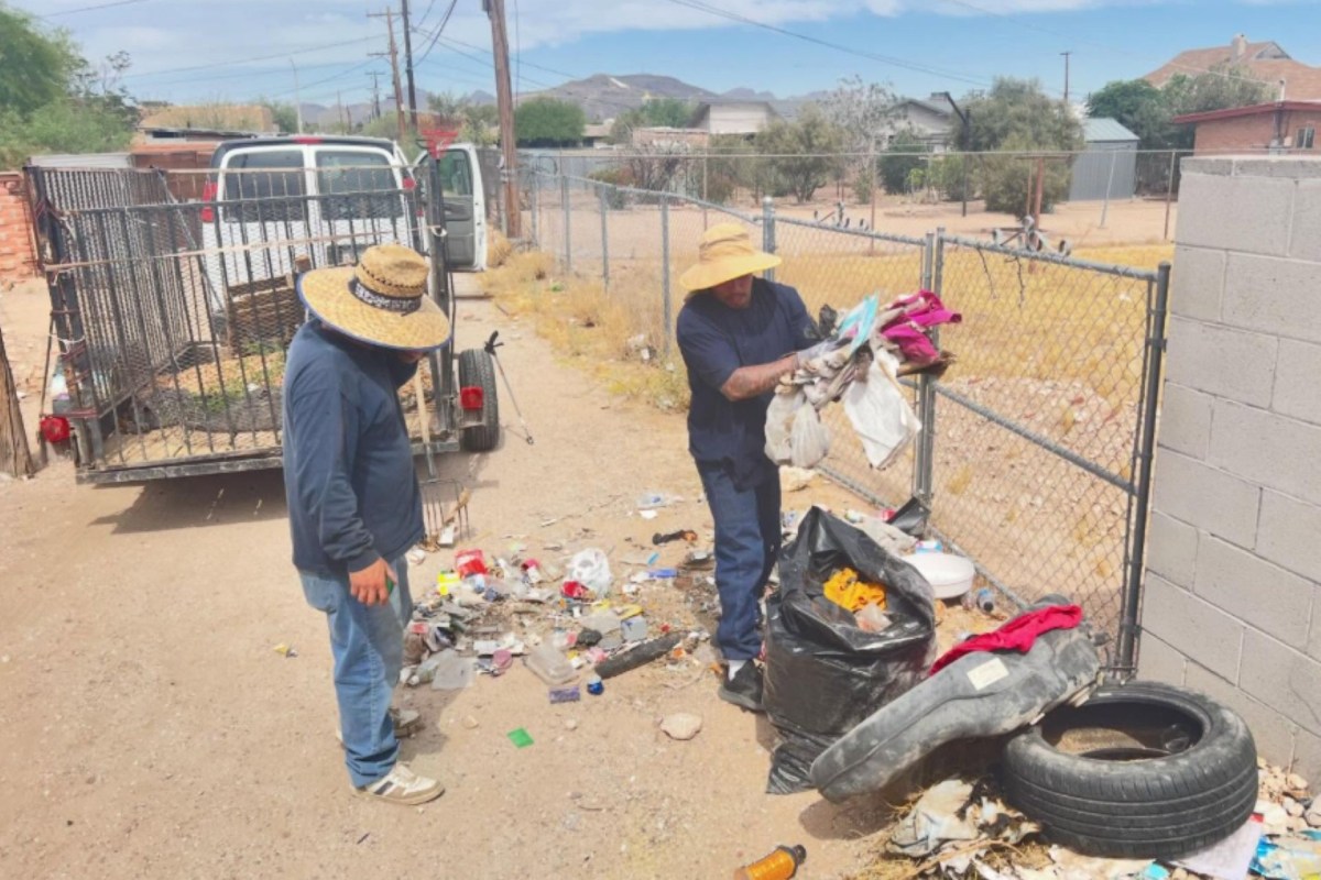 Two men wearing straw hats are cleaning up garbage in an outdoor area filled with trash and debris.