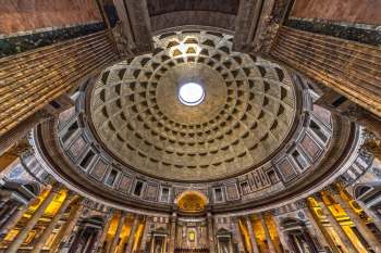 The intricate dome of a grand ancient building features a central oculus and ornate columns surrounding the interior.