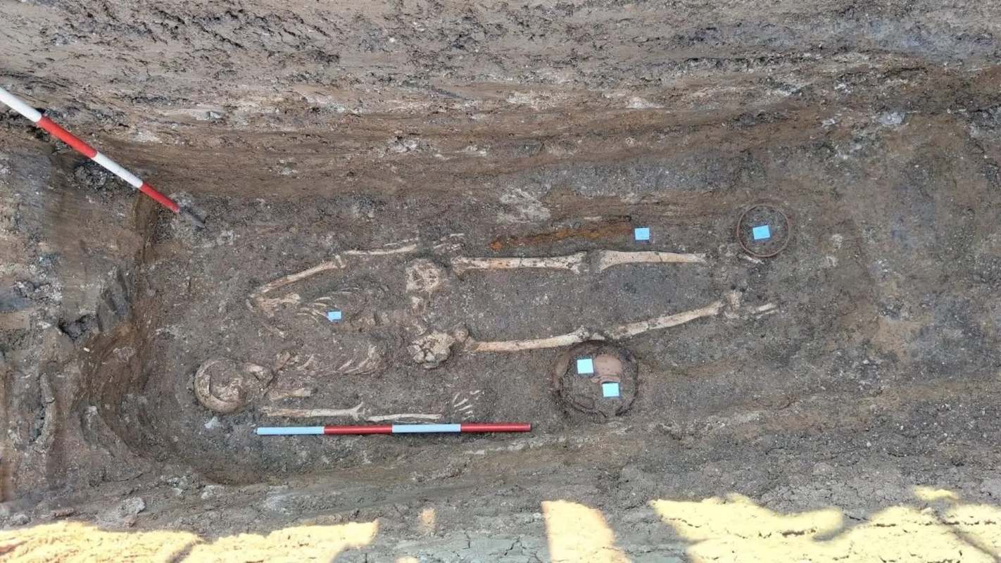 An archaeological site revealing a skeleton surrounded by artifacts and measuring tools in dirt.