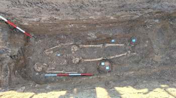 An archaeological site revealing a skeleton surrounded by artifacts and measuring tools in dirt.