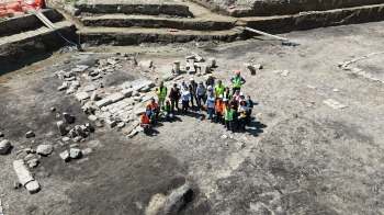 A group of archaeologists poses together at a dig site surrounded by stone structures and excavation areas.