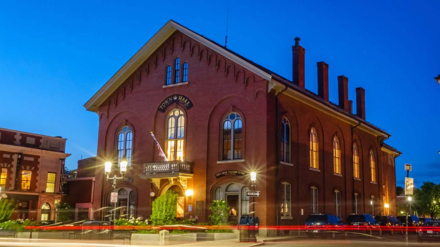 A brick town hall illuminated at dusk.