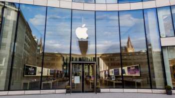 A modern Apple Store with large glass windows reflecting the surrounding buildings and a prominent Apple logo.