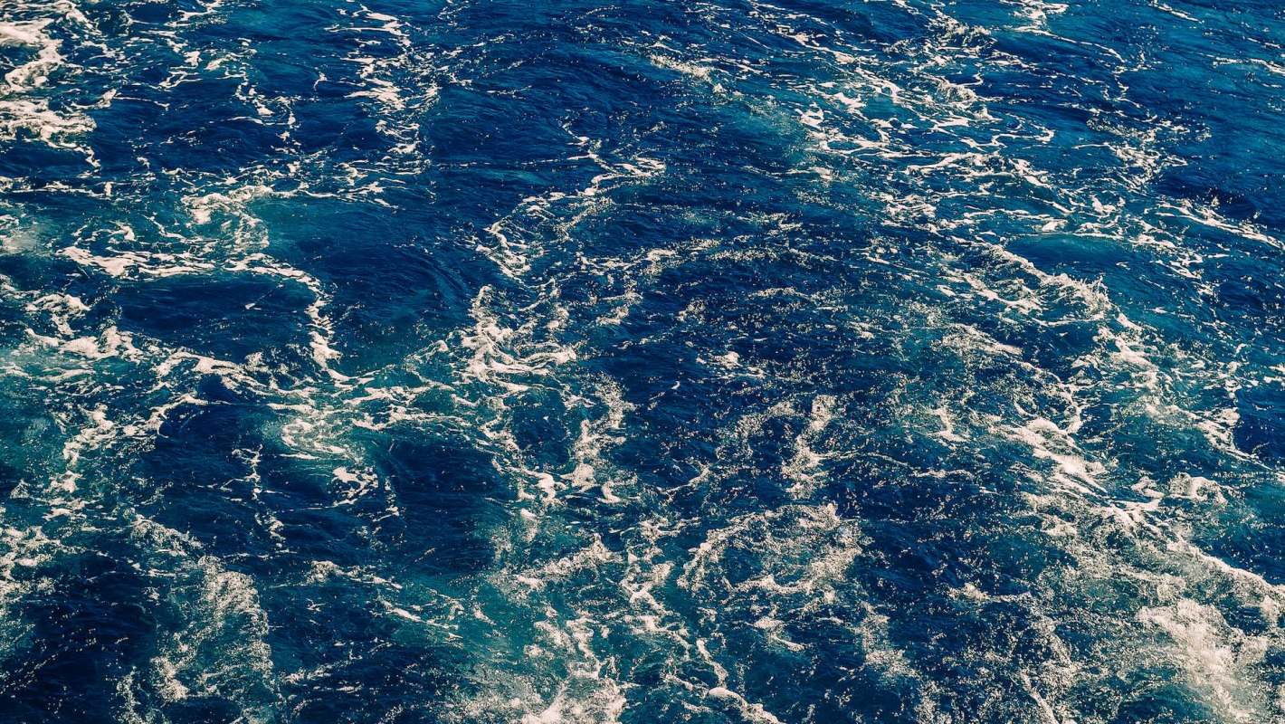A close-up view of blue ocean water with white foamy waves and ripples.