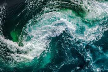Aerial view of turbulent ocean water with swirling waves and varying shades of blue and green.