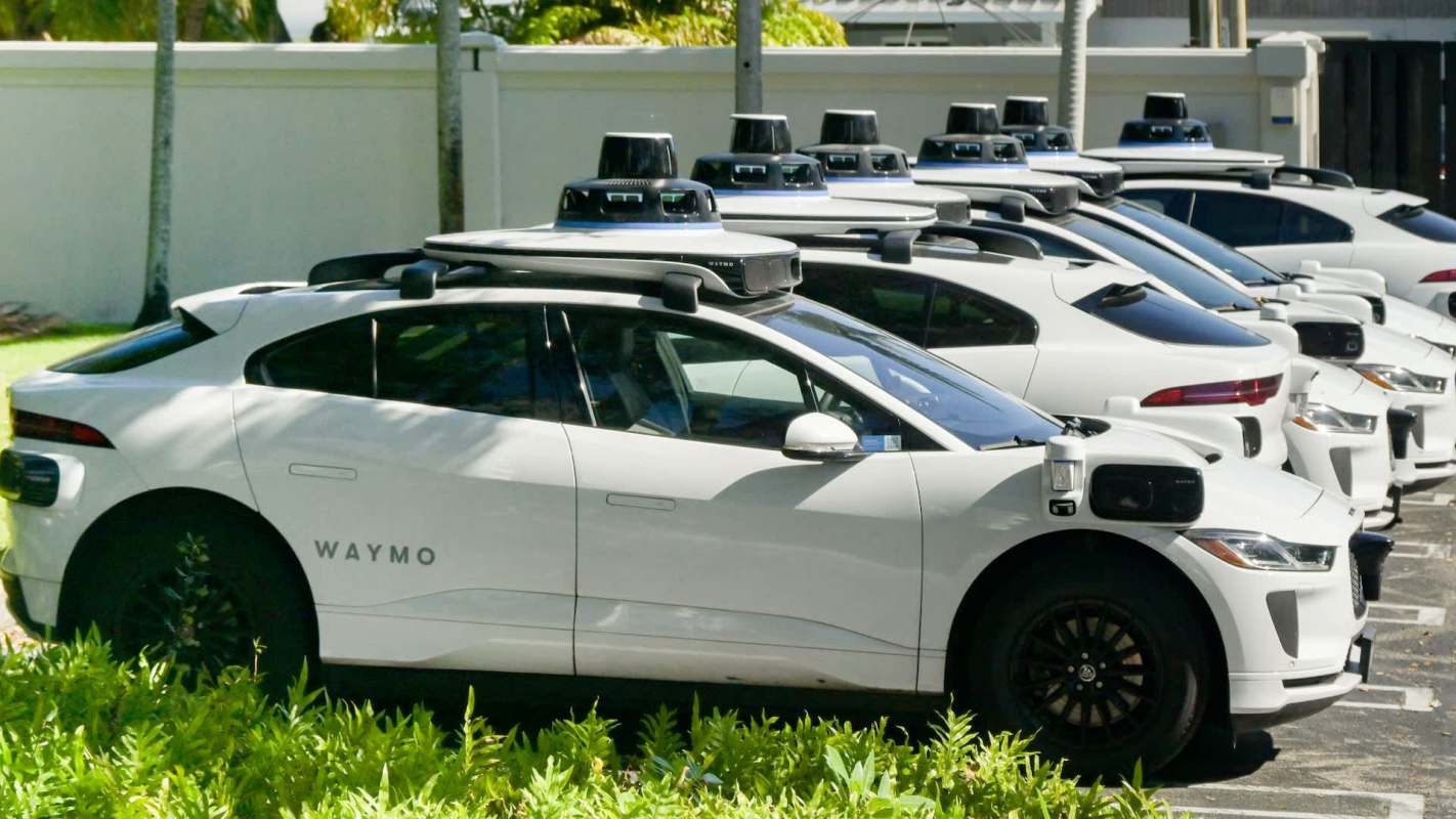 A row of Waymo's white autonomous electric vehicles parked outside.