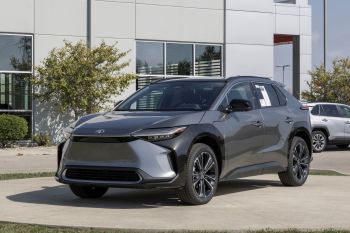 A sleek gray Toyota electric SUV parked outside a dealership with a modern building in the background.