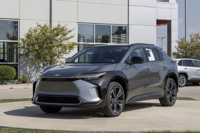 A sleek gray Toyota electric SUV parked outside a dealership with a modern building in the background.