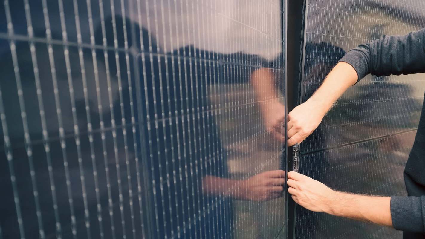 A person is aligning and securing a solar panel with their hands, showcasing the panel's reflective surface.