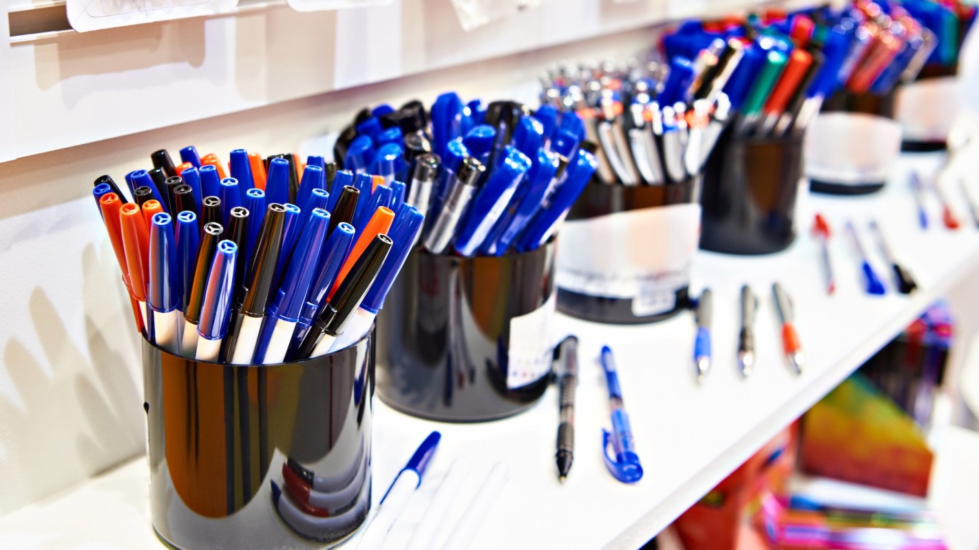 A collection of colorful pens organized in black containers on a white shelf.