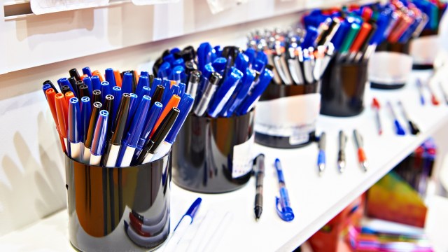 A collection of colorful pens organized in black containers on a white shelf.