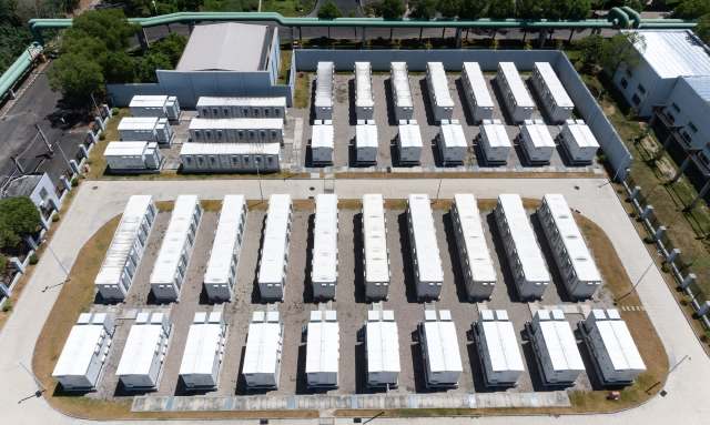 Aerial view of a battery energy storage system with white containers in rows on a gravel surface.