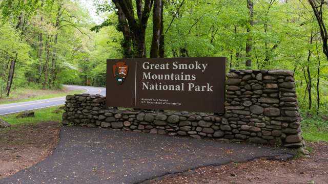 A wooden sign for Great Smoky Mountains National Park stands at the entrance, surrounded by lush green trees.