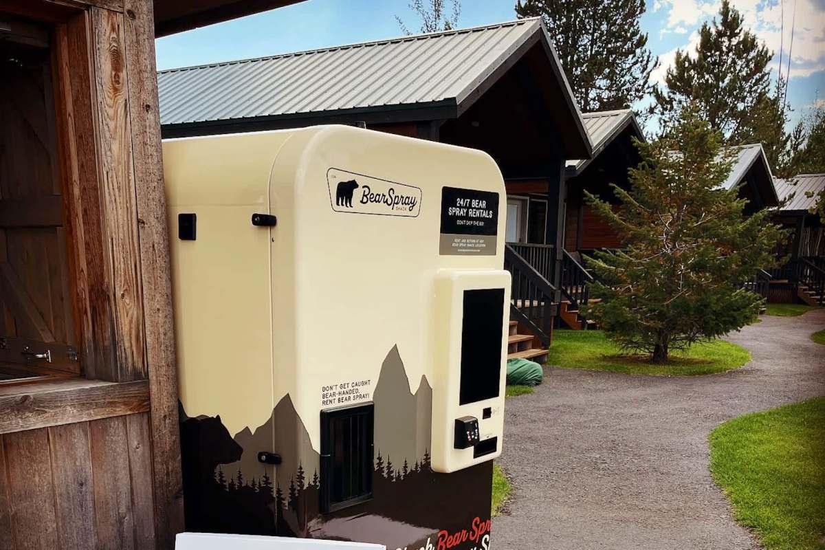A bear spray rental kiosk located near wooden cabins in a forested area.