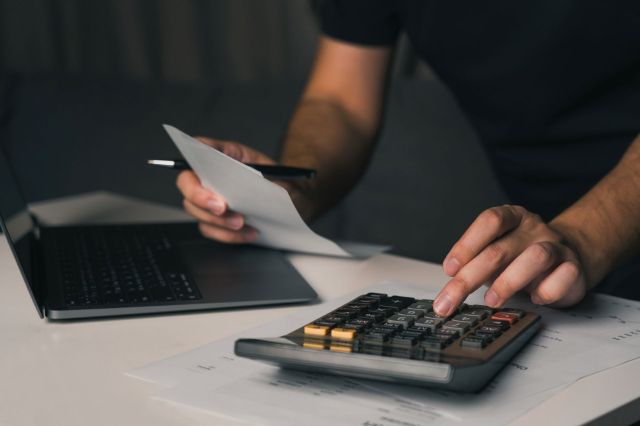 A person using a calculator and laptop.