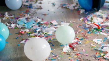 A messy floor strewn with colorful confetti, streamers, and balloons after a celebration.