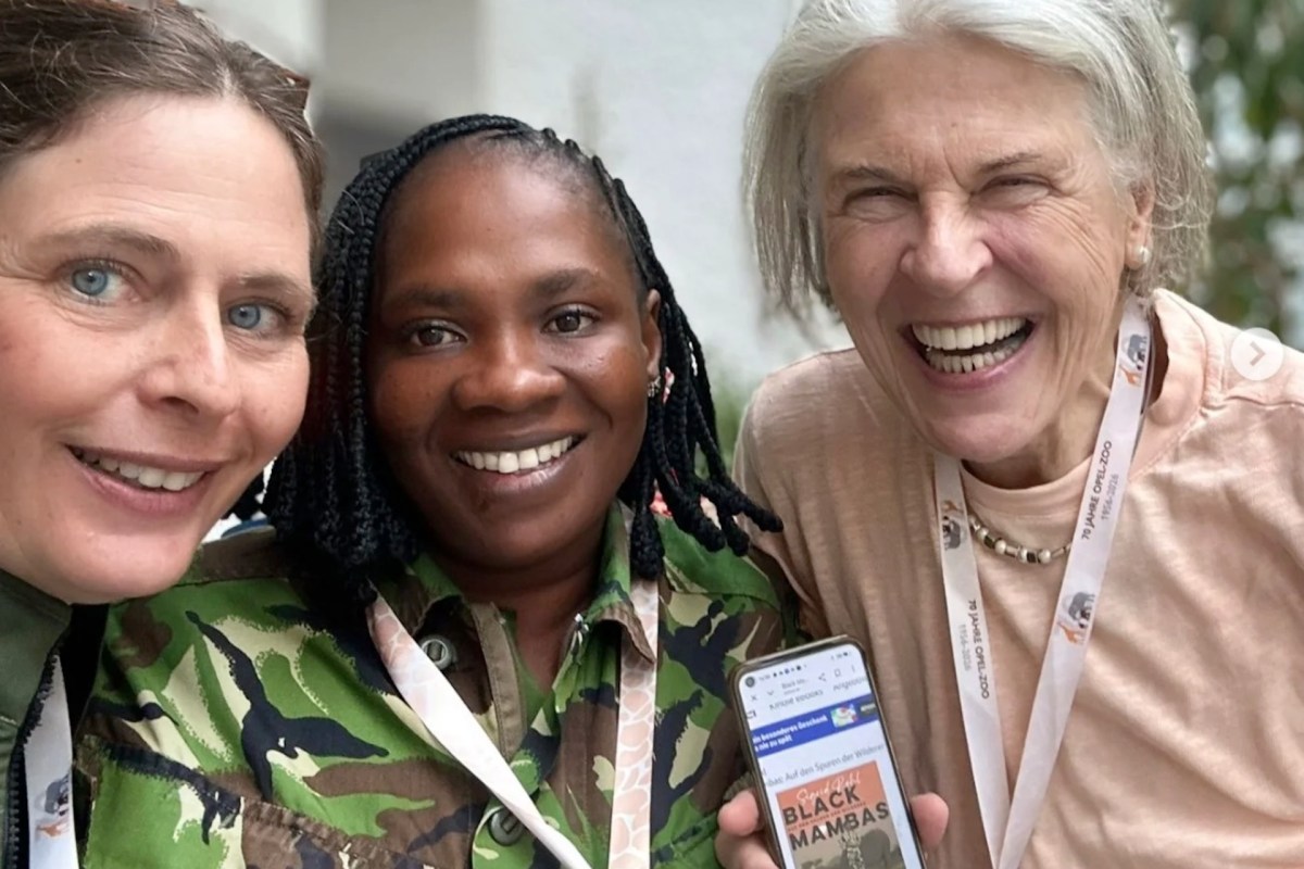 Three women smile together in a selfie, one holding a phone displaying information about "Black Mambas."