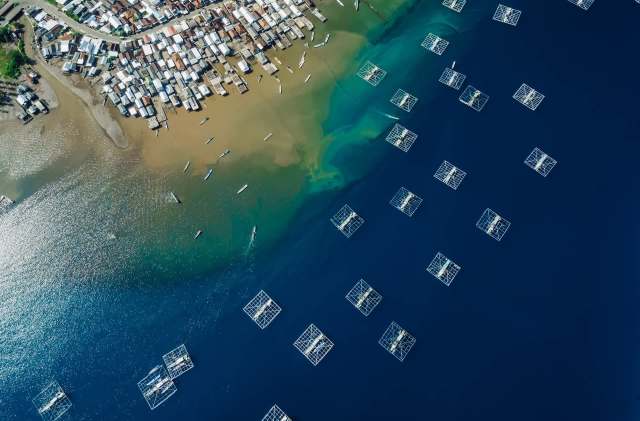 A coastal village with colorful houses beside water with fish farming cages.