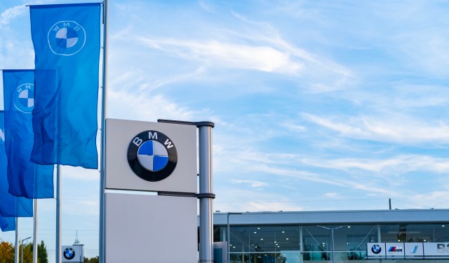 A BMW dealership with flags and a prominent logo set against a clear blue sky.