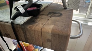 A wooden cutting board with visible grooves and a black bowl of pink food on a marble countertop.