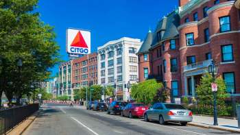 A Boston city street lined with historic buildings and the iconic large CITGO sign under a clear blue sky.
