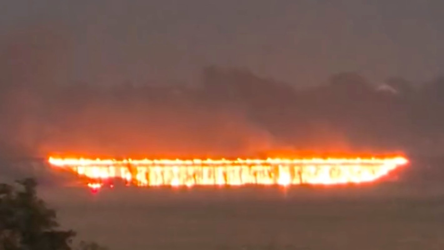 A long, fiery line on the horizon, surrounded by dark smoke from a bridge burning.