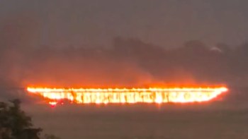 A long, fiery line on the horizon, surrounded by dark smoke from a bridge burning.