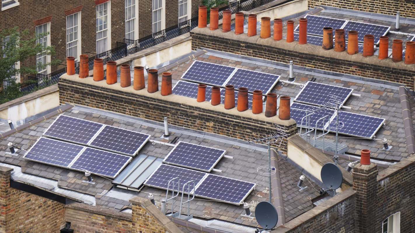 Rooftops featuring solar panels and numerous red clay chimneys in an urban setting.
