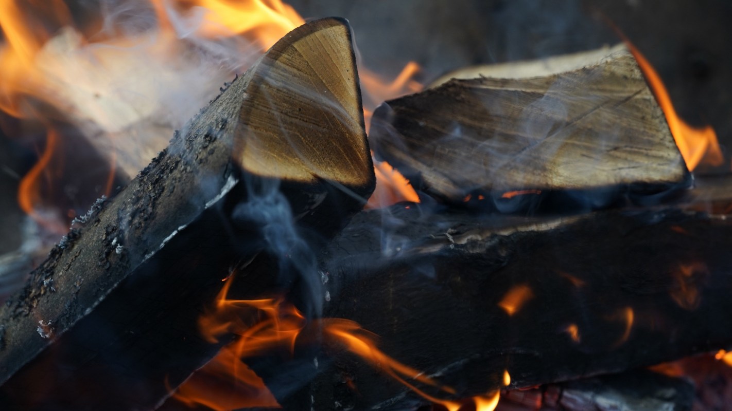 Close-up of burning logs with glowing embers and swirling smoke.