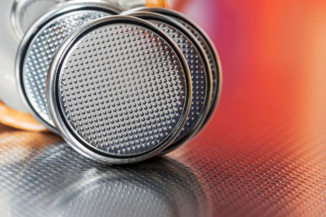 Close-up of several silver button batteries with dotted surfaces resting on a textured metallic background.