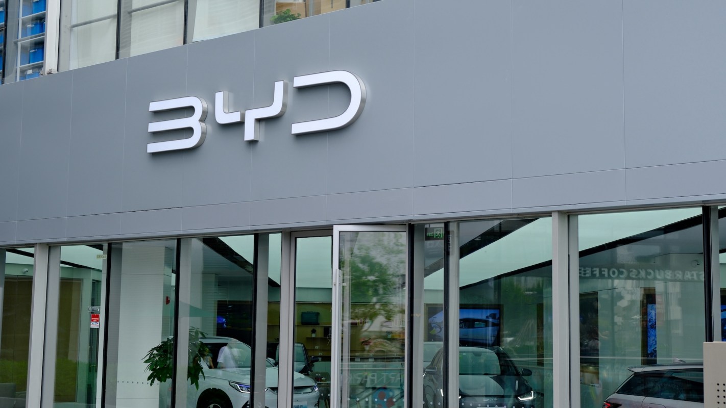 A close-up of a BYD dealership exterior with the company logo and displayed vehicles visible through large windows.