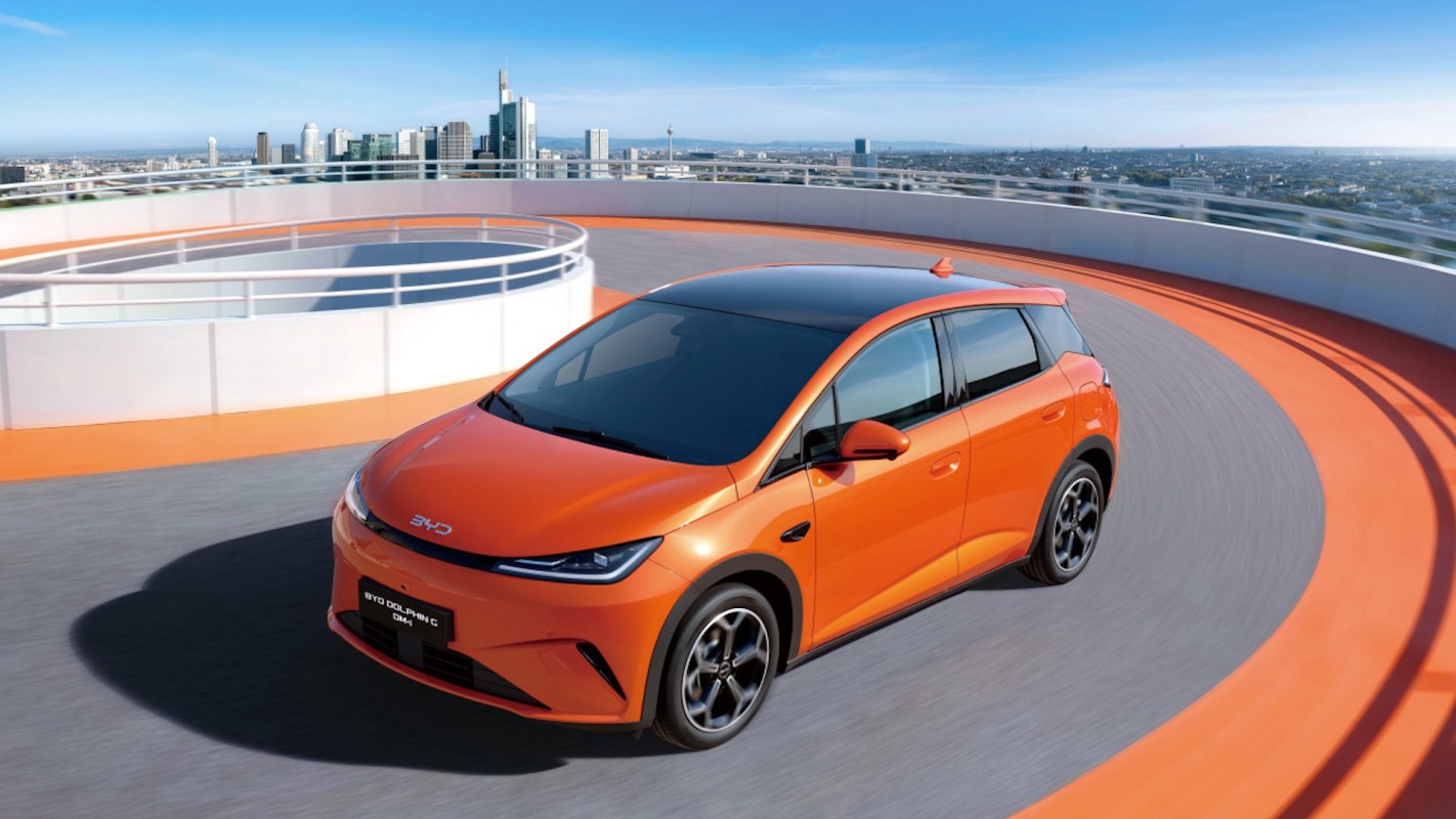 An orange electric car navigates a curved racetrack in front of a cityscape.