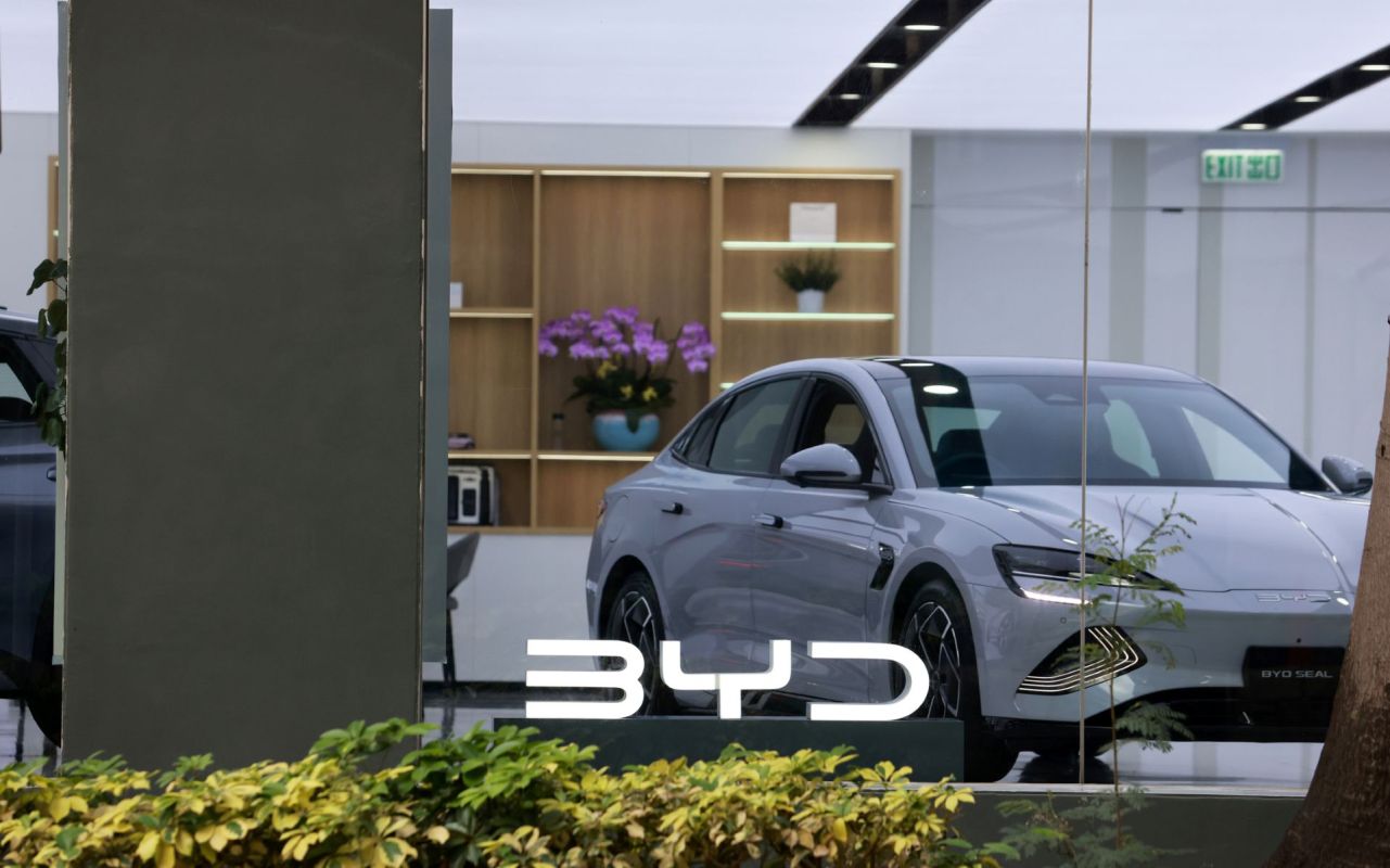 A silver BYD Seal car displayed in a showroom with plants and modern decor in the background.