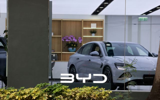 A silver BYD Seal car displayed in a showroom with plants and modern decor in the background.
