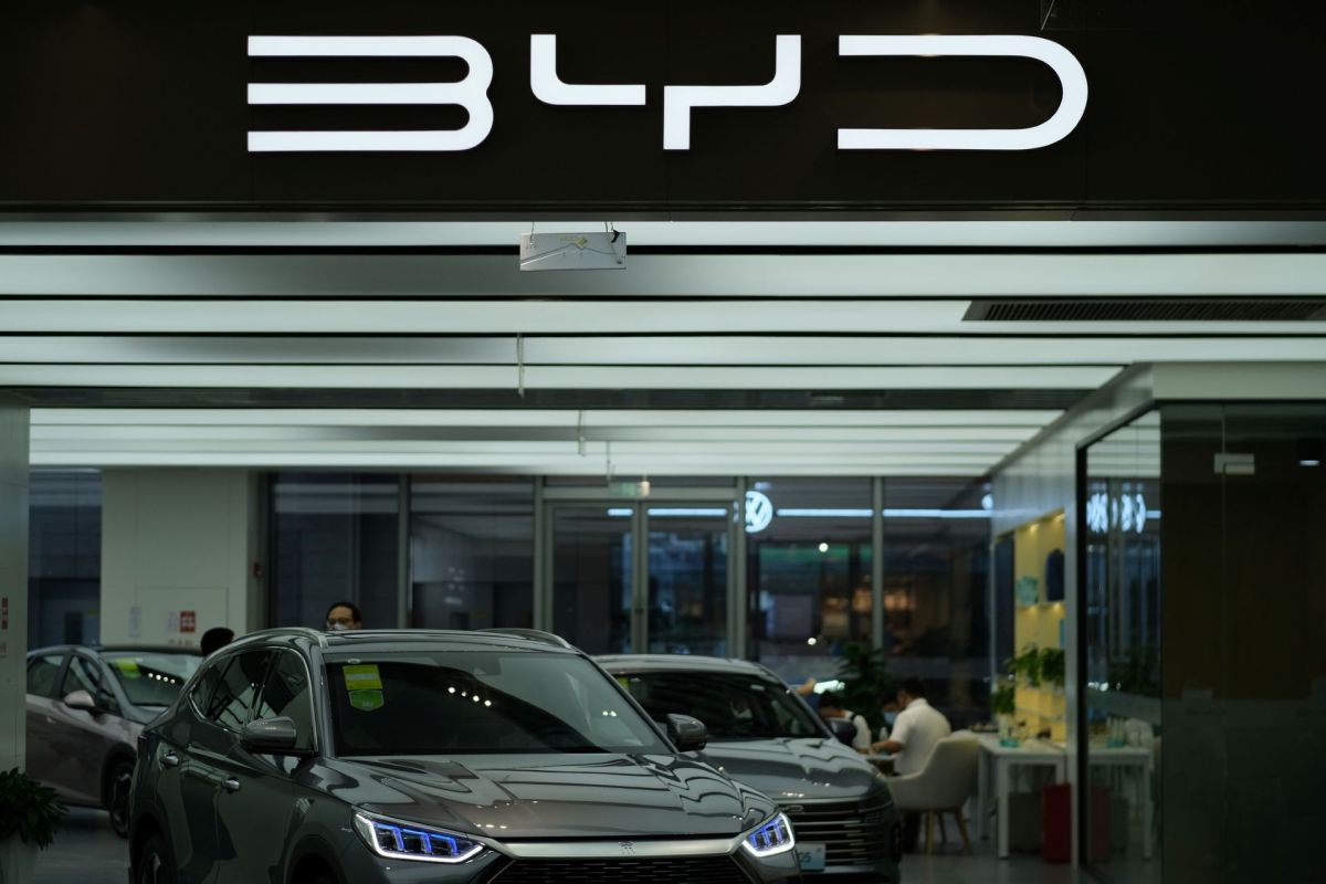 A modern car showroom displaying several vehicles, including a gray SUV, with the BYD logo prominently featured.