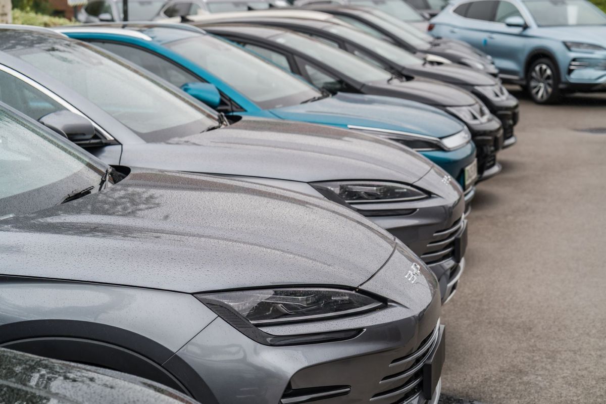 A row of parked vehicles with rain-soaked hoods, featuring various shades of grey and a blue car in the background.