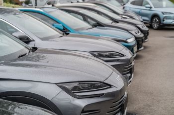 A row of parked vehicles with rain-soaked hoods, featuring various shades of grey and a blue car in the background.